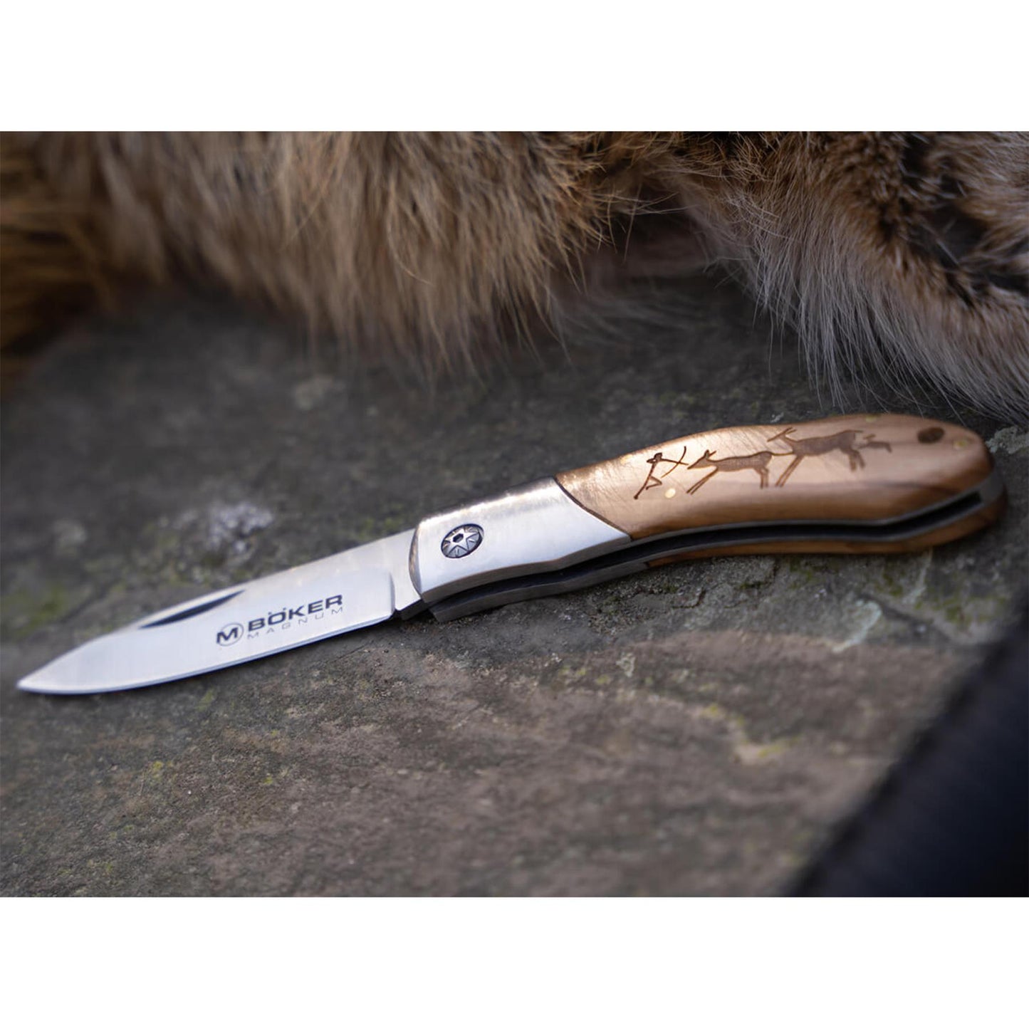 Boker Magnum Caveman sulankstomas peilis su medine rankena, papuosta medžiokles scena, ir plieno geležte ant akmens