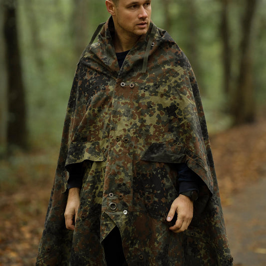 Vyras miške dėvi vandeniui atsparų Vokietijos kariuomenės Flecktarn kamufliažo palapinės pončą.